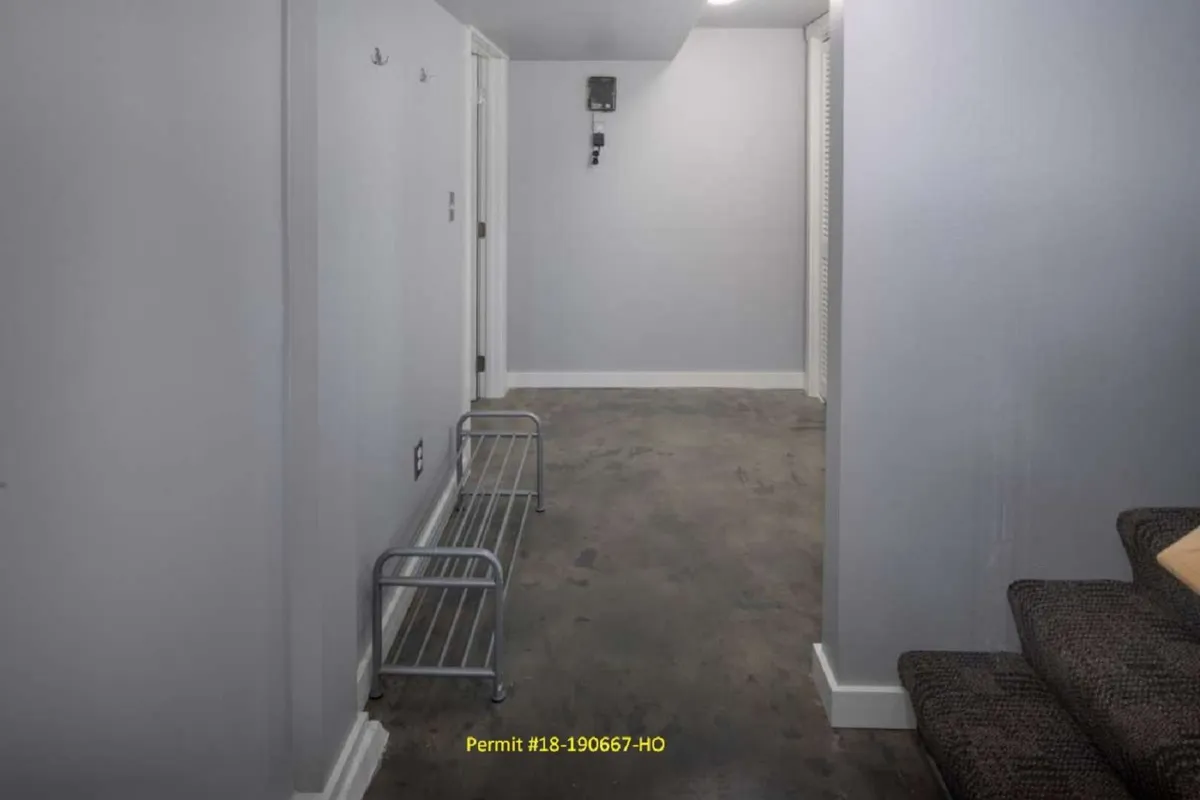 A functional, well-lit interior space showcasing a metal rack, walls, flooring, and a doorway. The elements suggest a space designed for arriving home, storing shoes and bags, and organizing oneself upon entry.