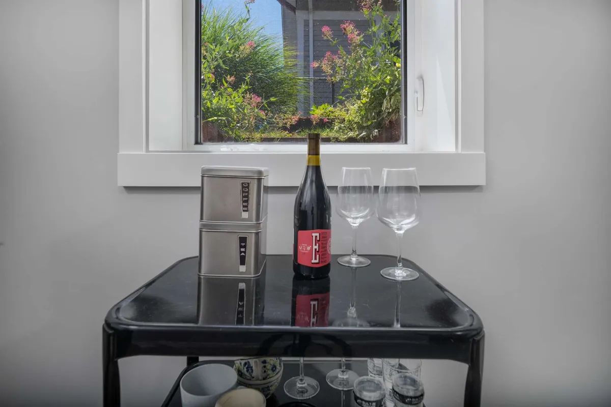 A stylish spot by a window with a wine bottle and glasses arranged for a casual tasting, featuring views outside and subtle storage elements. The mood is one of easy elegance, perfect for unwinding with friends or sharing a leisurely drink.