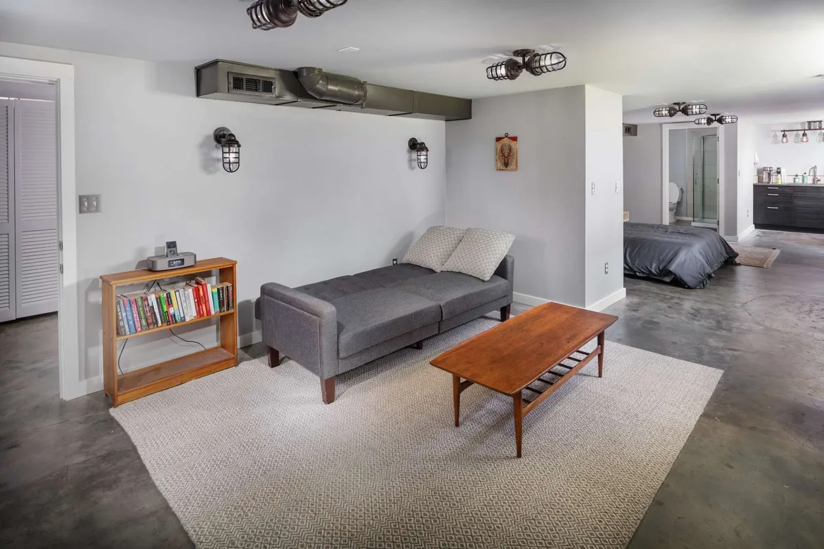 A cozy, open-concept living room featuring a comfortable sofa, a central coffee table, a bookshelf, and stylish lighting fixtures. The space is bright, casual, and arranged to encourage both relaxation and social interaction, with ample seating for small groups.