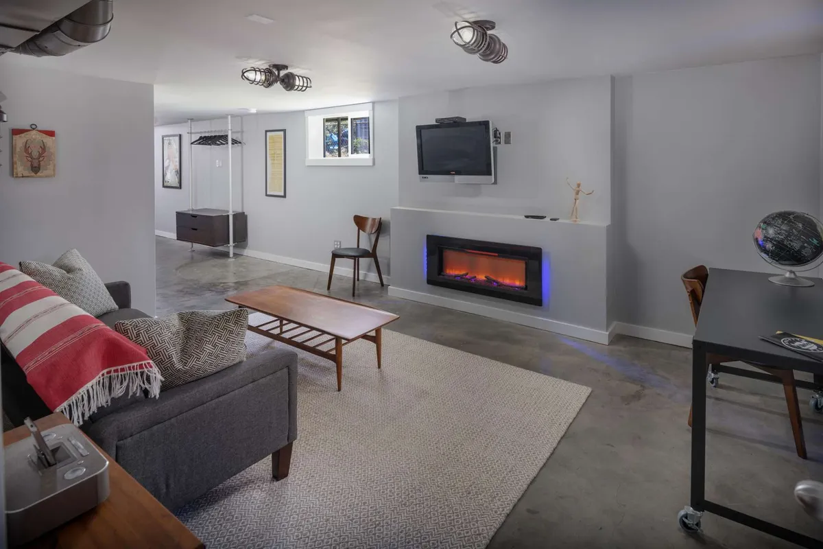 The image showcases a stylish, inviting living area featuring a plush sofa draped with a vibrant red and white throw blanket, a sleek modern fireplace, a warm wooden coffee table ideal for gatherings, a wall-mounted TV, and a cozy desk with a globe, all set in a bright, contemporary space.
