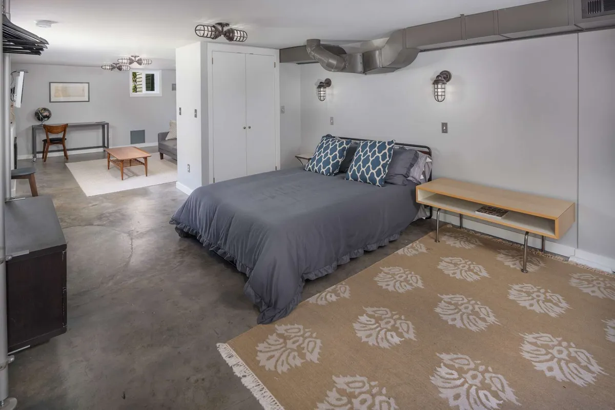 A warm, inviting interior space with a bed adorned in gray bedding and decorative pillows, a floral-patterned rug, and a wooden side table. The atmosphere is calm and perfect for unwinding, reading, or intimate conversation.